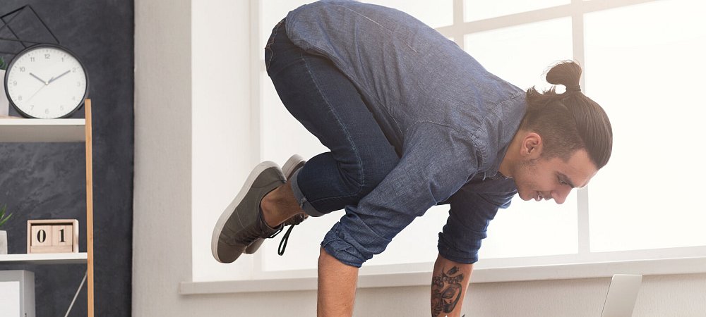 Short break for yoga in office. Flexible man practicing yoga at workplace, making balance exercise on desk, copy space. Active employee at work, healthy lifestyle concept